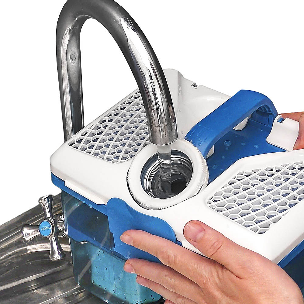 THOMAS AquaBOX, pouring water from the tap through the lid opening THOMAS AquaBOX water filter. Tap water is poured into the blue plastic container through the opening in the closed lid